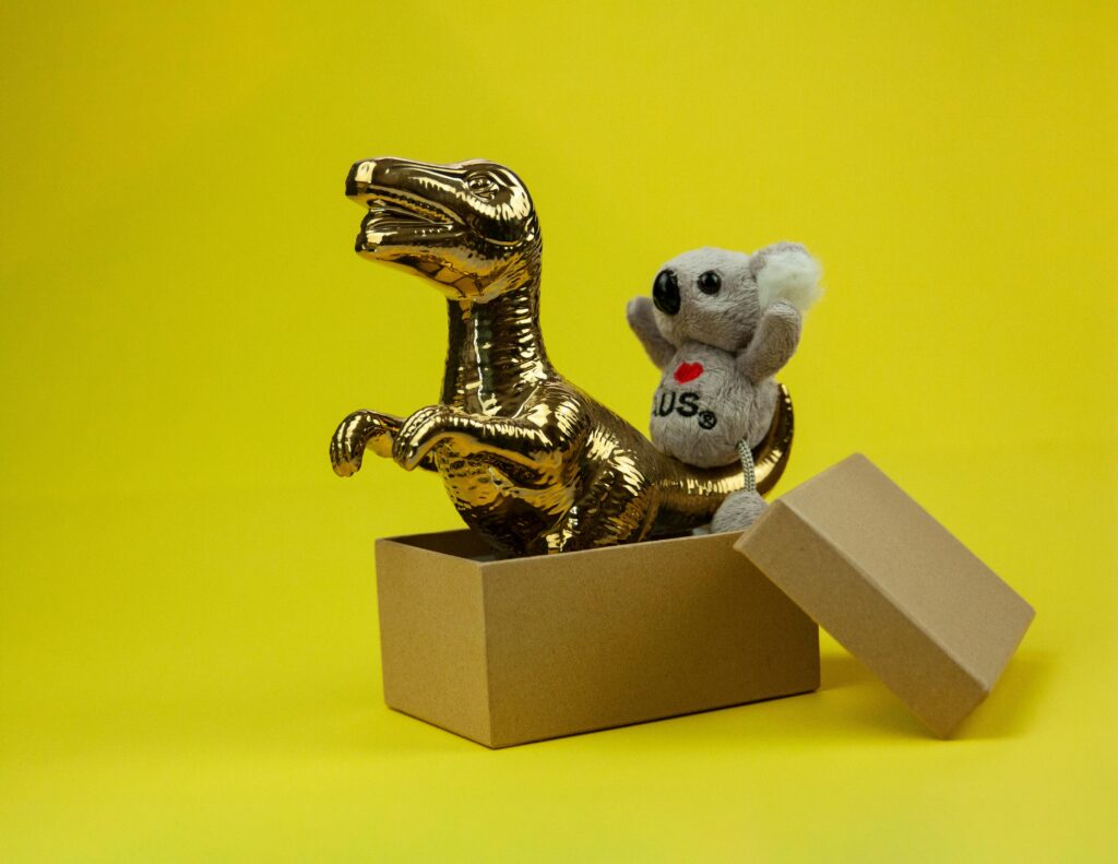 A golden dinosaur and koala toy in an open box with a vibrant yellow backdrop.